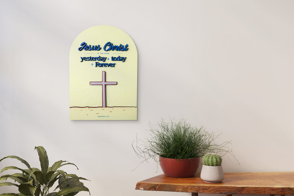 3D wooden Christian wall decor featuring the phrase 'Jesus Christ is the same yesterday, today, and forever,' with a cross illustration and the Bible verse Hebrews 13:8, displayed above a table with potted plants.