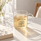 Clear glass mug with Always with you, it will be okay Christian illustration, filled with tea on a bright sunlit table.