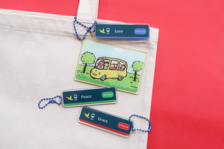 Singapore-inspired Christian acrylic keychains on a tote bag featuring Jesus Loves Me transport card, Love, Peace, and Grace MRT sign designs