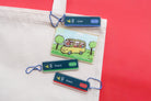 Singapore-inspired Christian acrylic keychains on a tote bag featuring Jesus Loves Me transport card, Love, Peace, and Grace MRT sign designs