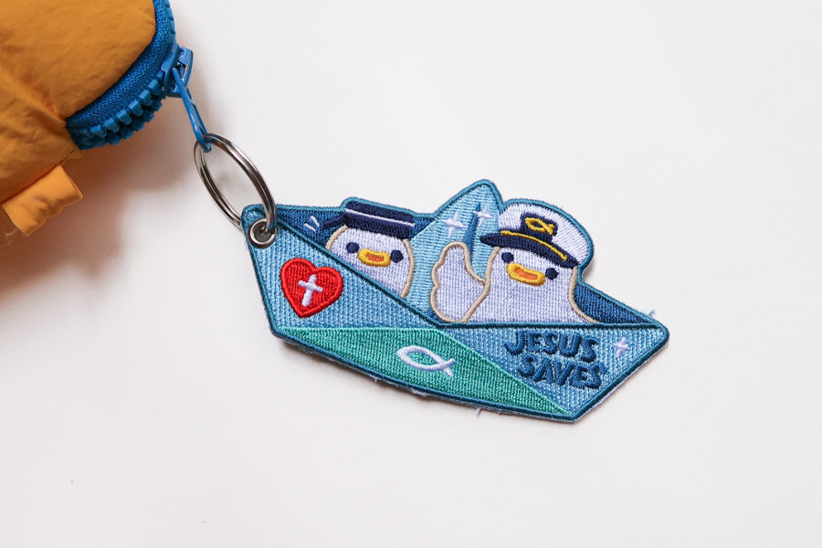 Jesus Saves embroidered Christian keychain featuring cute sailor characters in a paper boat design clipped onto zipper.