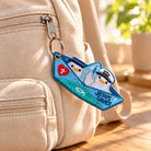 Jesus Saves embroidered Christian keychain hanging naturally from a beige backpack zipper in warm sunlight.