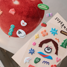 Close-up of Soft Jesus and Superman sticker sheets, featuring colorful and inspirational designs.
