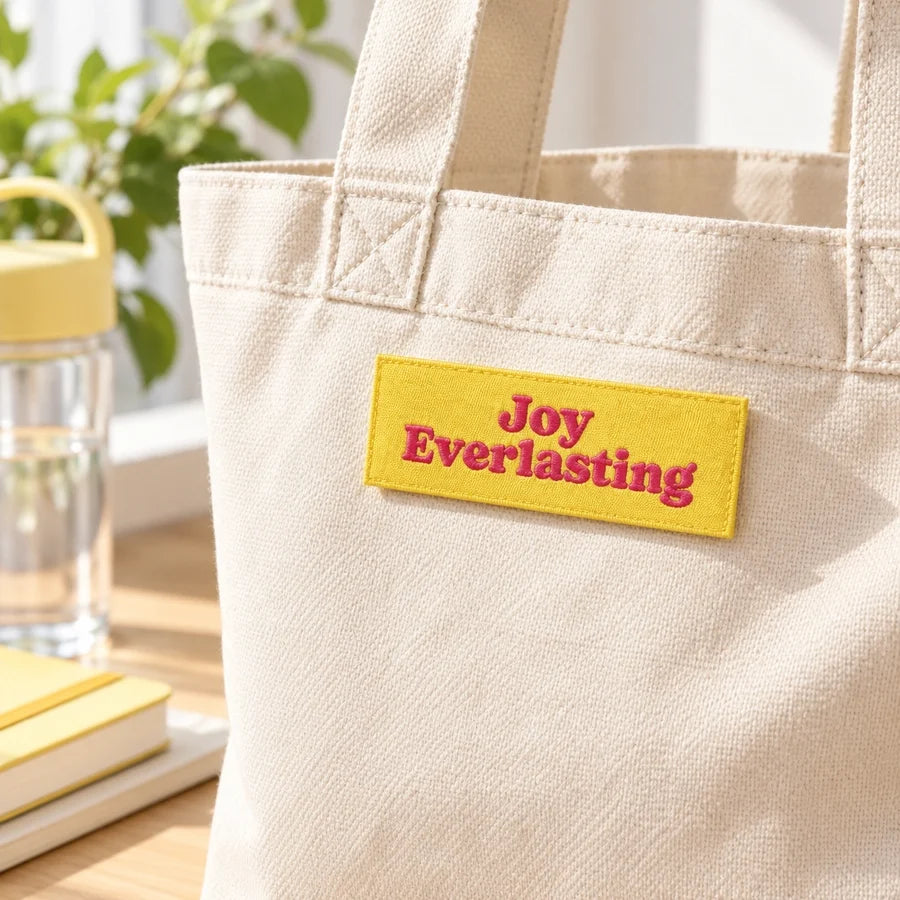 Joy Everlasting pink-lettered yellow Velcro patch attached to a cream canvas tote bag