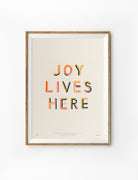Joy Lives Here Christian poster in a light wood frame