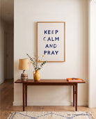 Keep Calm and Pray Christian poster displayed above a wooden console table in a warm neutral entryway