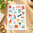 Kingdom Everyday Stickers sticker sheet styled on a desk with notebook, pencil, greenery and coffee.