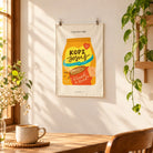 Kopi Jesus Coffee small wall tapestry clipped to a sunlit wall above a wooden table.