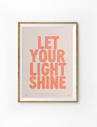 Let Your Light Shine Christian poster with warm coral lettering displayed in a wooden frame on a white background