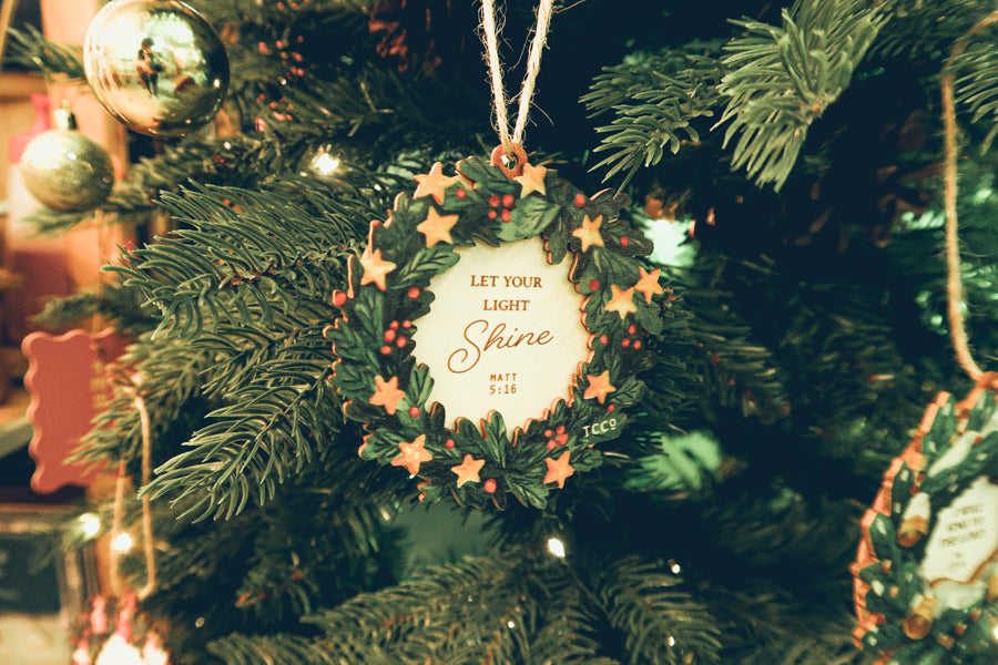 'Let Your Light Shine' Christmas wreath ornament with stars and holly berries, beautifully hanging on a decorated Christmas tree with festive lights.