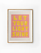 Let Your Light Shine Christian poster with yellow lettering on a pink background displayed in a wooden frame
