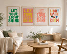 Pink and yellow Let Your Light Shine poster displayed with colourful Christian posters in a bright living room