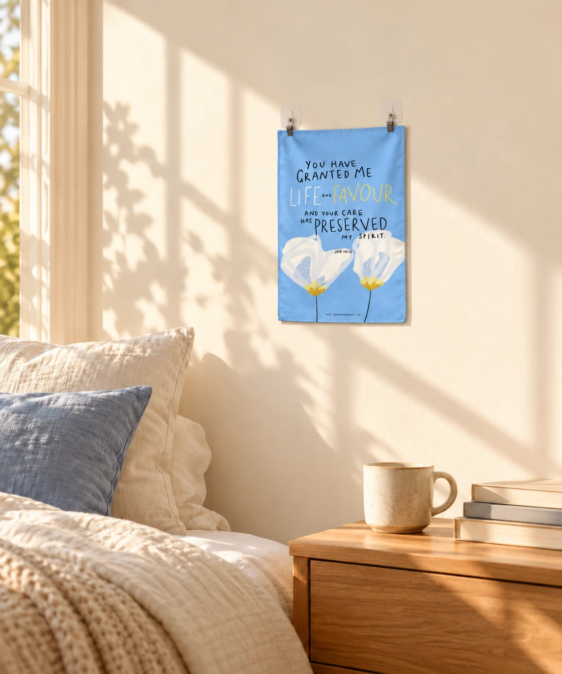 Life and Favor blue wall tapestry displayed above a cosy bedside table in warm natural light