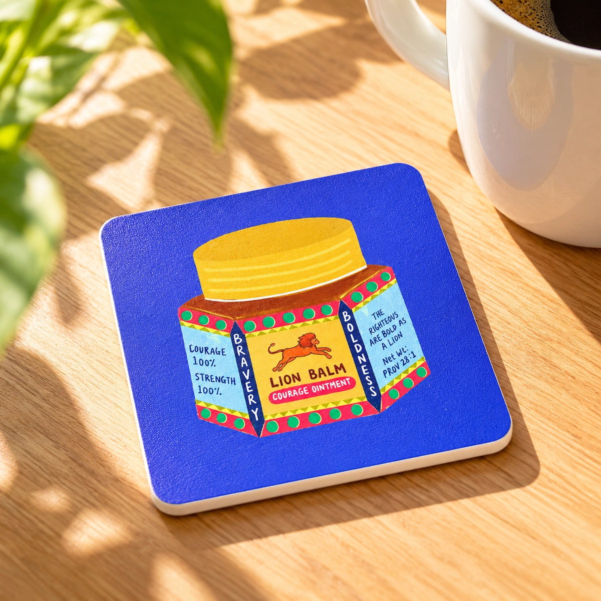 Lion Balm Proverbs 28:1 Christian coaster styled on a sunlit wooden table beside a coffee mug.