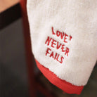 Love Never Fails embroidered cotton towel product view.