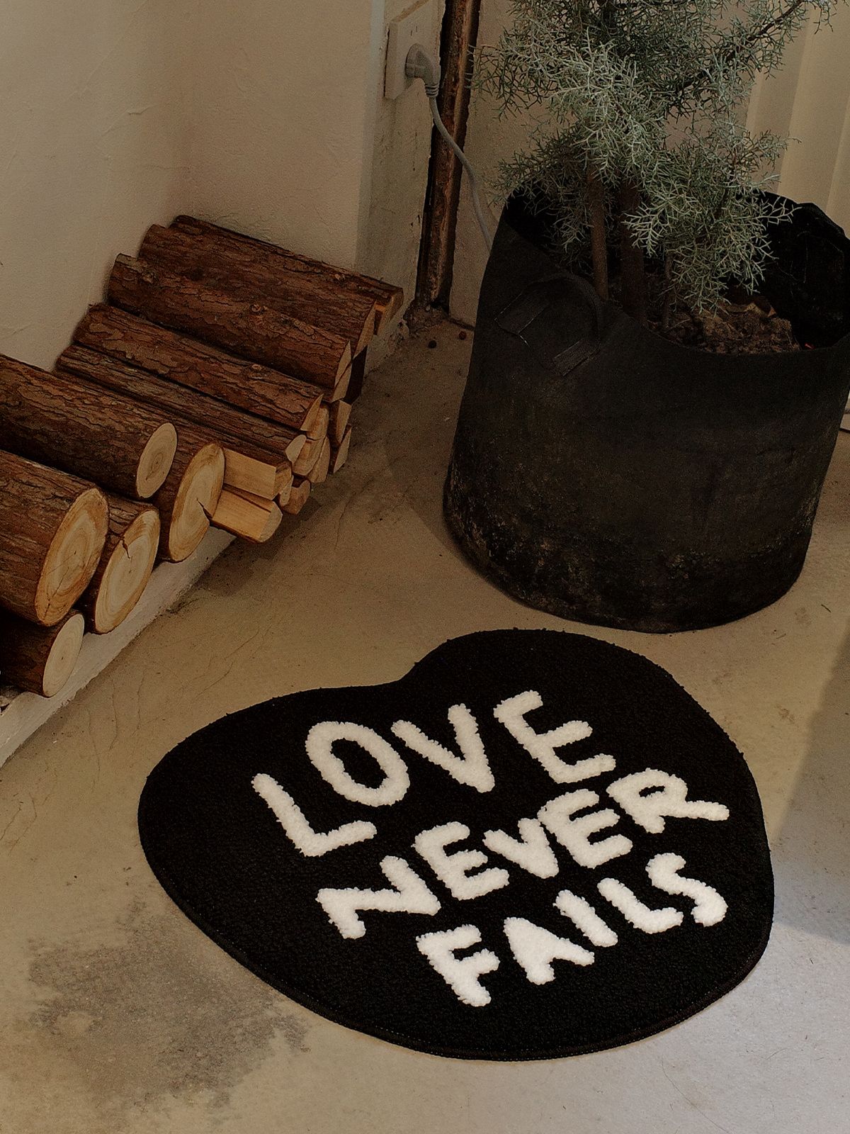 Top-down view of the Love Never Fails heart-shaped rug showing white tufted text on a black background.