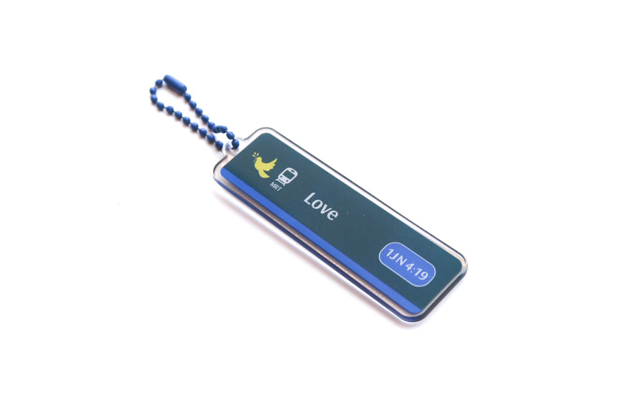 Angled view of Singapore-inspired Train Station Love acrylic keychain with 1 John 4:19 verse reference