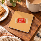 Loved by the Father coffee biscuit Christian coaster from the LOVE SUPERMARKET collection on a warm wooden table.