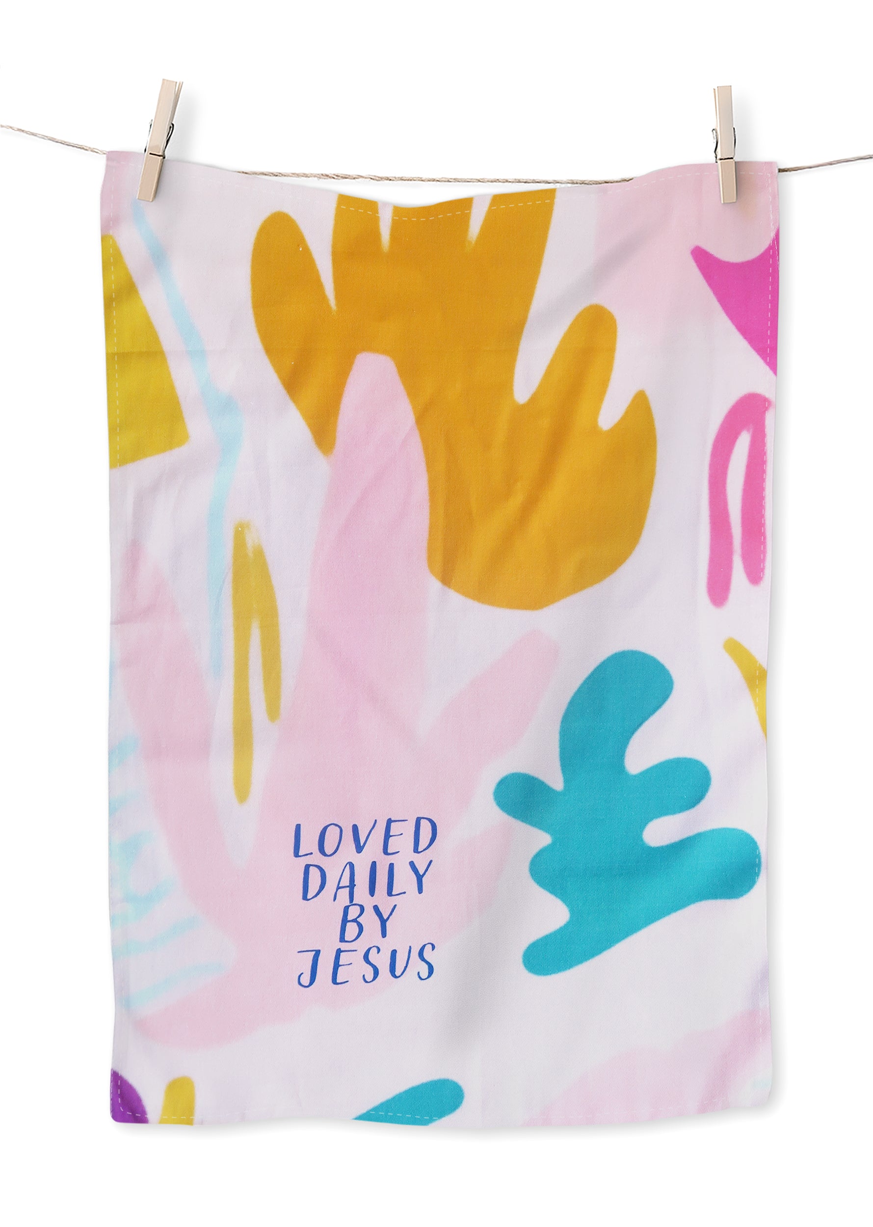 Colorful abstract tea towel with pink, yellow, and blue shapes and the phrase "LOVED DAILY BY JESUS" in blue; a Christian home decor gift from The Commandment Co.