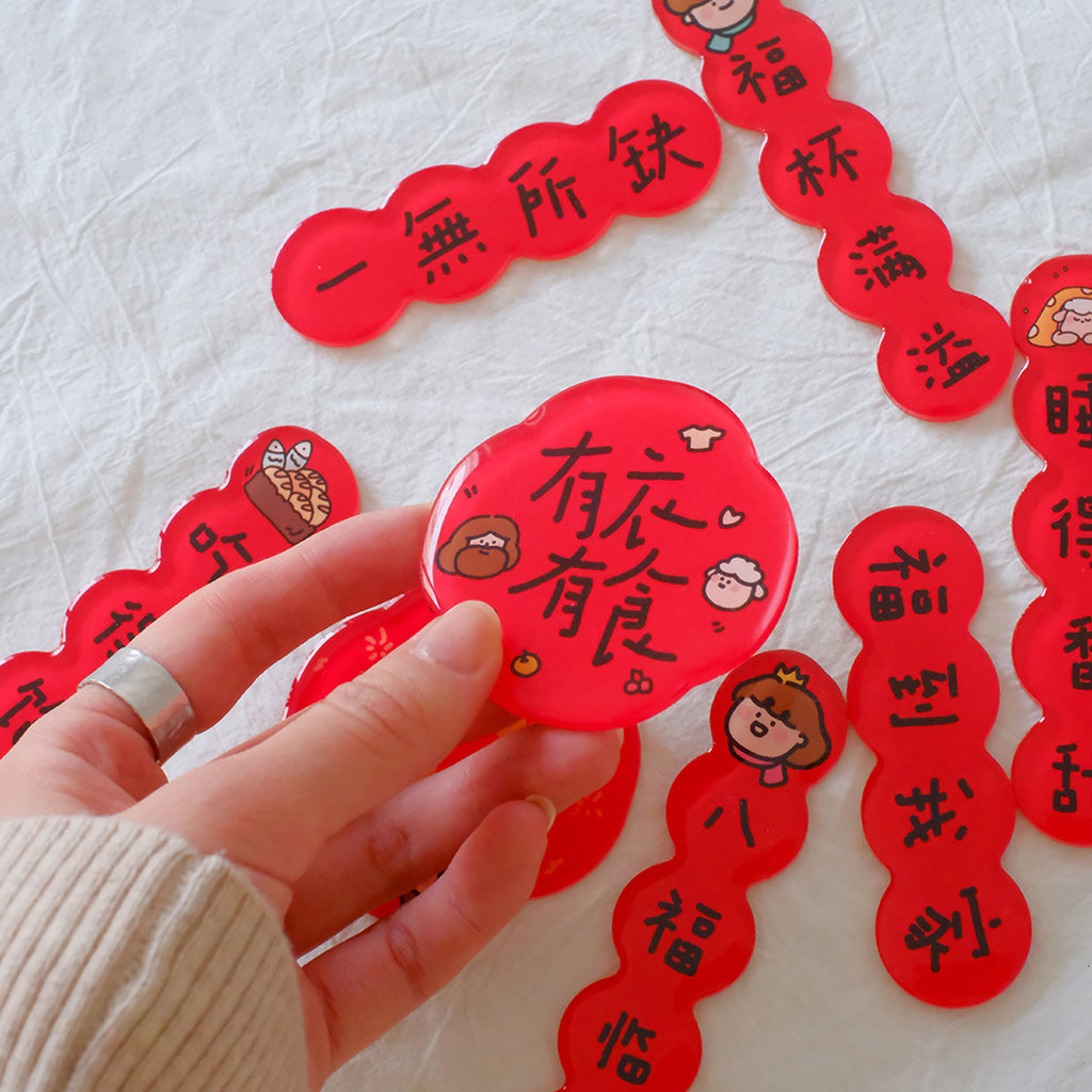 Close-up of Chinese New Year couplet magnets in red with festive blessings, featuring inspirational designs and held by hand.