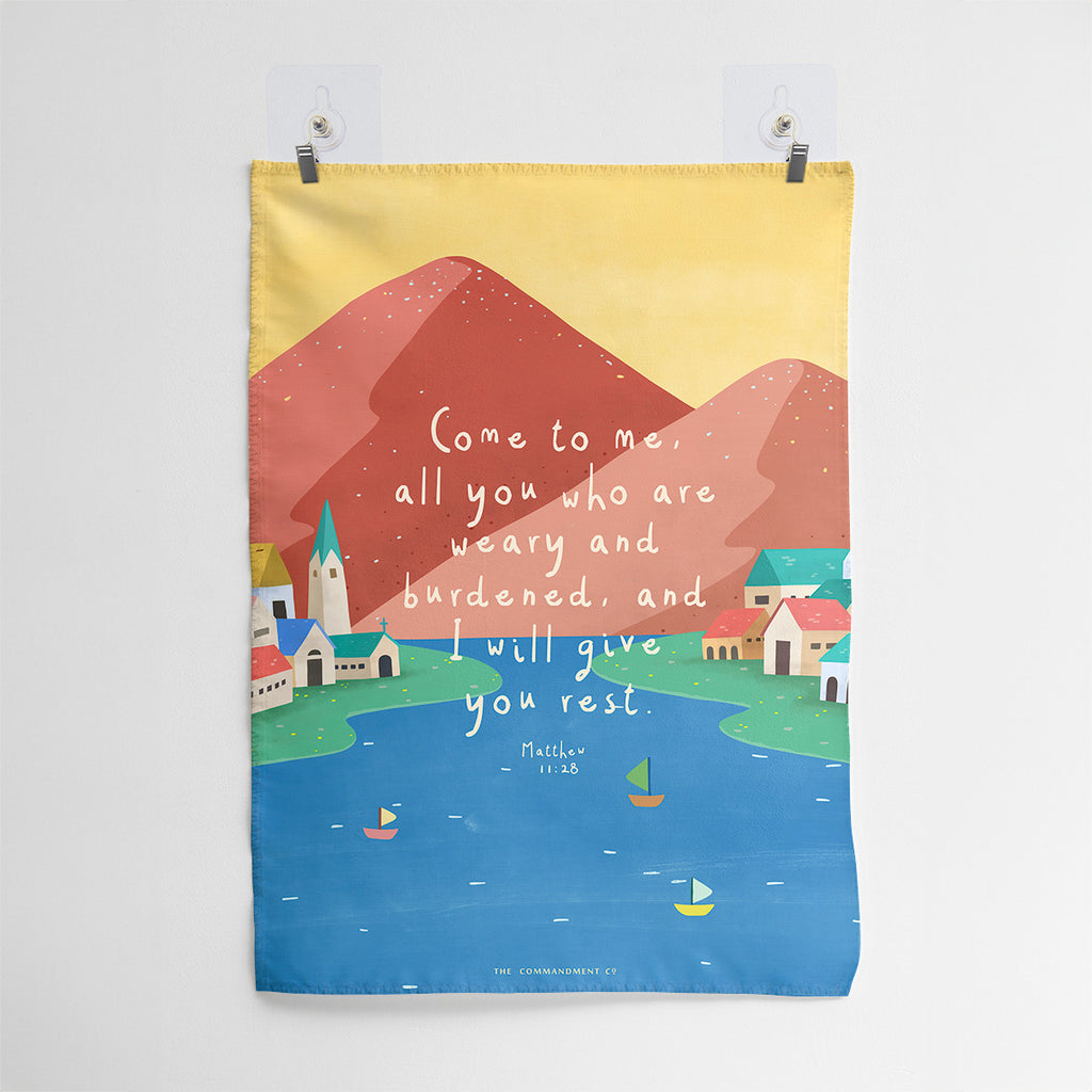 Christian wall art featuring Matthew 11:28, 'Come to me, all you who are weary and burdened, and I will give you rest,' with a colorful landscape of mountains, a village, and a serene lake.