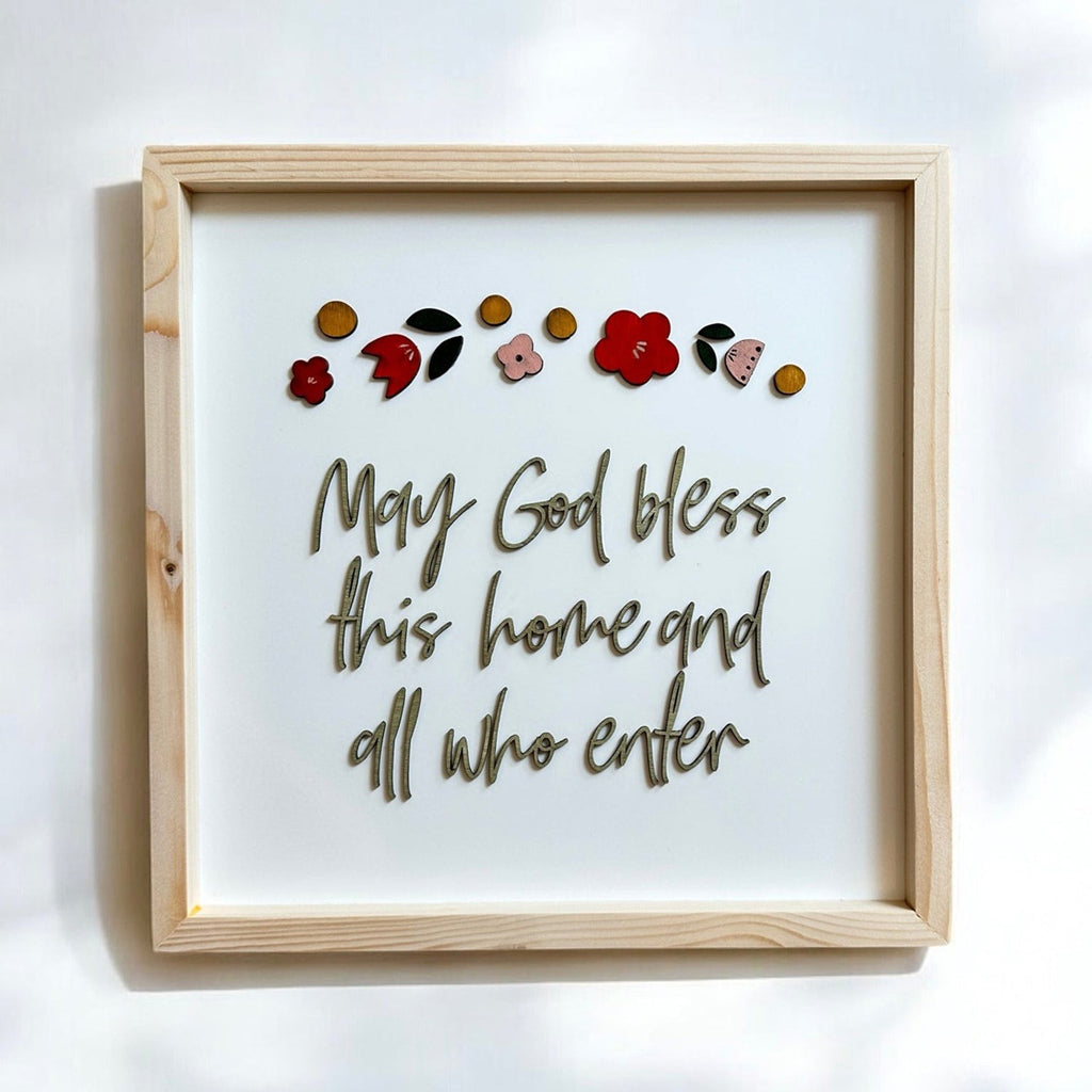 Faith-inspired wooden-framed wall art featuring the quote 'May God bless this home and all who enter,' decorated with red flowers and colorful accents.