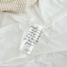 Clear glass mug with the handwritten message "Maybe you are dissatisfied with yourself from time to time. Actually, you have done a great job," placed on a soft white blanket, inspiring encouragement and simple happiness.
