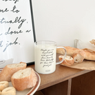 Clear glass mug with the encouraging message "Maybe you are dissatisfied with yourself from time to time. Actually, you have done a great job," filled with milk and surrounded by fresh bread, inspiring self-love and simple happiness.