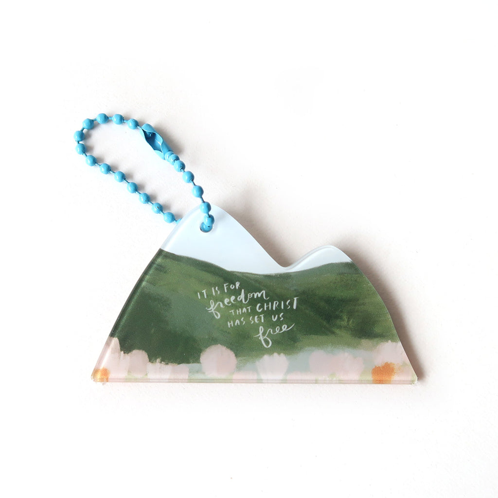 Mountain-shaped Christian keychain featuring the quote 'It is for freedom that Christ has set us free' with a floral background and a blue chain.