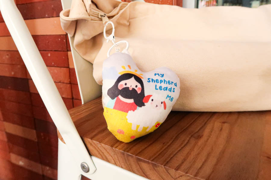 A plush keychain featuring an illustration of Jesus with a sheep, accompanied by the phrase 'My Shepherd Leads Me,' symbolizing faith and guidance.