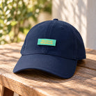 Navy blue Christian baseball cap with a mint-green The Good Shepherd velcro patch displayed on a rustic wooden table.