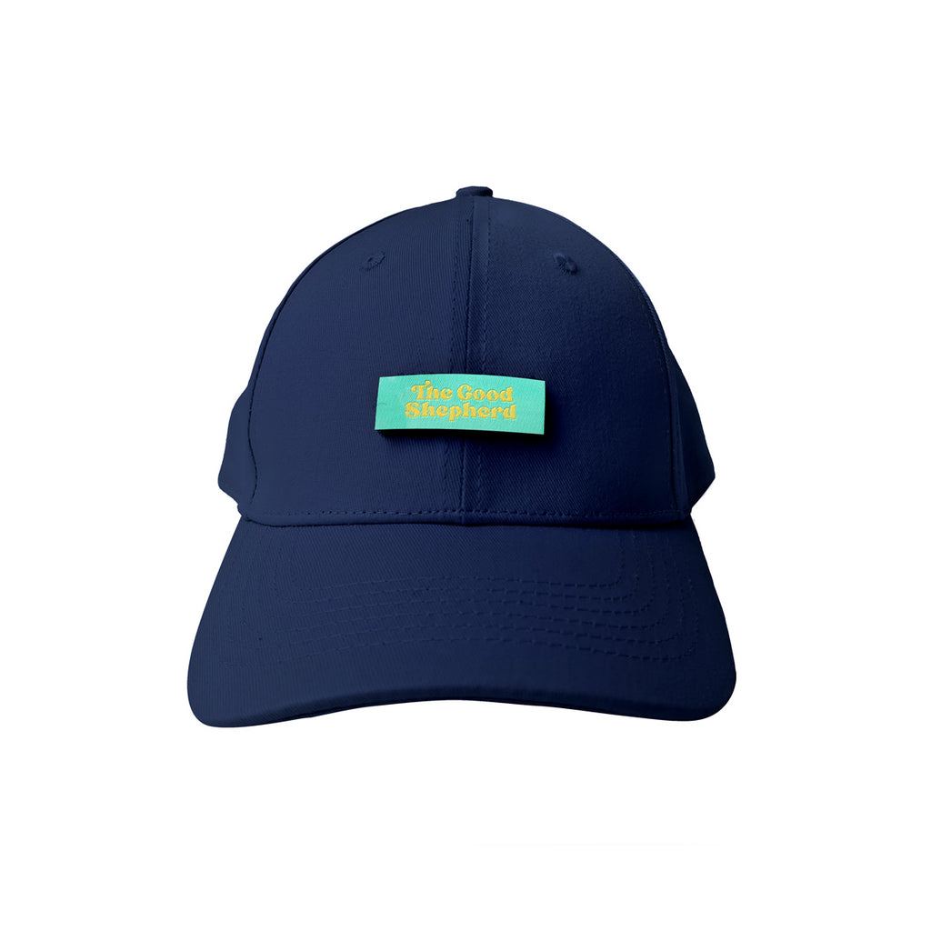 A navy blue cap featuring a turquoise patch with yellow text reading "The Good Shepherd," a Christian-inspired accessory promoting faith and positivity.