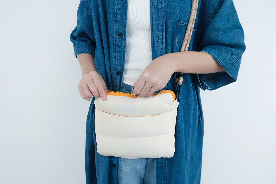 Person opening the oat-colored multi-purpose bag, showing its durable zipper and padded texture.