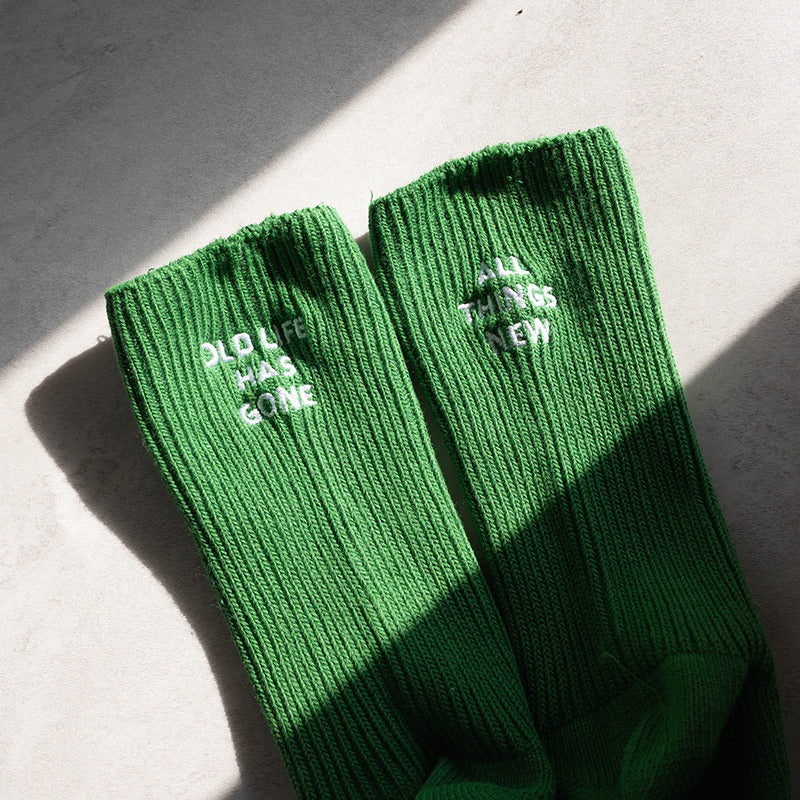 Green ribbed socks with white embroidered text reading 'Old Life Has Gone' and 'All Things New' on paired socks, a faith-inspired reminder of renewal.