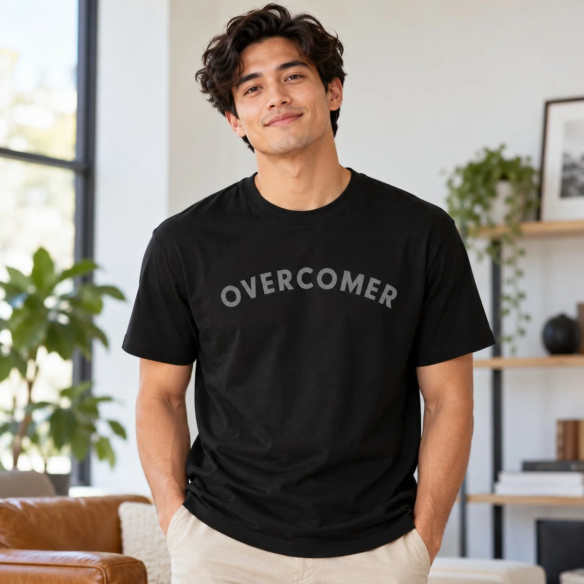 Lifestyle photograph of a man wearing a black Overcomer faith-inspired T-shirt indoors.