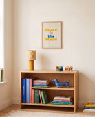 Peace Is the Mood Scripture poster displayed above a wooden bookshelf in a warm neutral room
