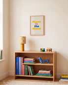 Peace Is the Mood Christian poster displayed above a wooden bookshelf in a warm neutral room
