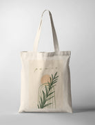 Minimalist Christian tote bag featuring the word “Peace” with abstract arches, soft peach sun, and green botanical leaves