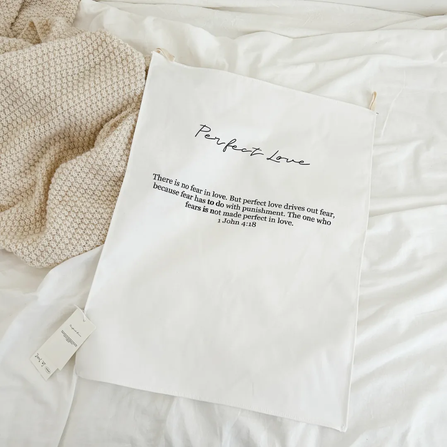 Minimalist "Perfect Love" wall tapestry featuring 1 John 4:18 Bible verse, displayed on a cozy bed with a knitted blanket, inspiring faith, comfort, and simple happiness.