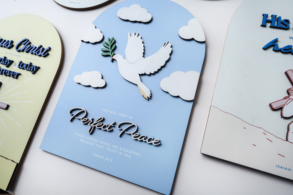 Close-up of a 3D wooden Christian poster featuring a white dove holding an olive branch, surrounded by clouds, with the phrase 'Perfect Peace' and the Bible verse Isaiah 26:3.