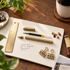 Personalised brass rollerball pen with stationery on a warm wooden desk