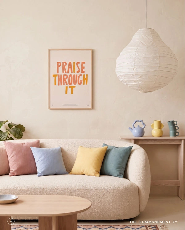 Praise Through It Christian poster displayed above a cream sofa in a warm living room