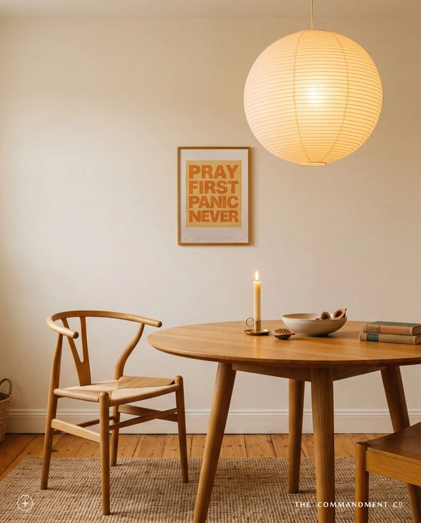 Pray First Panic Never Christian poster displayed above a wooden dining table in a warm neutral room