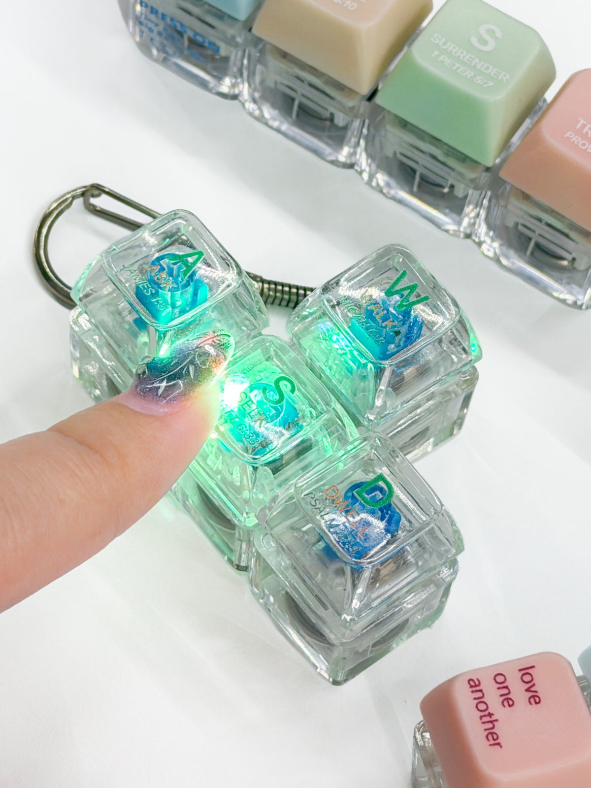 Press-on light-up Christian keycap keychains glowing when pressed, shown together on a bright tabletop