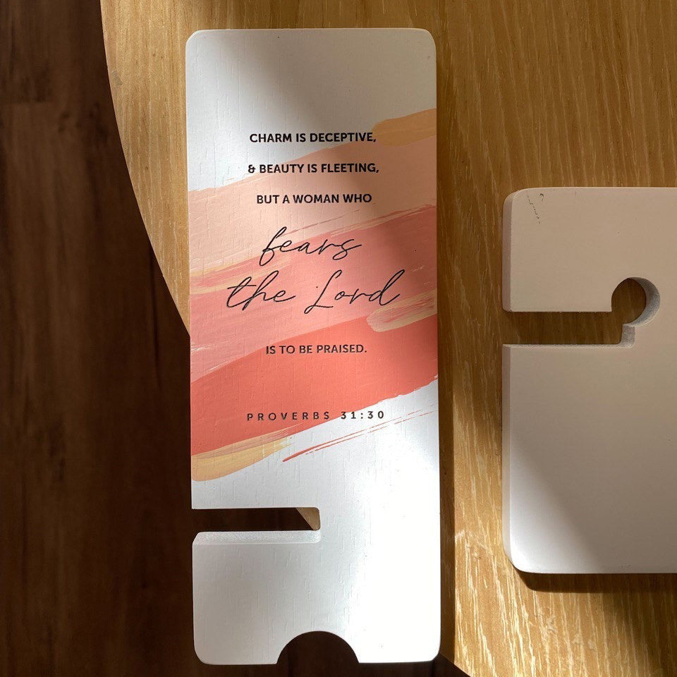 Wooden phone stand with Proverbs 31:30 Bible verse design, featuring the text 'Charm is deceptive, beauty is fleeting, but a woman who fears the Lord is to be praised,' on a red and orange painted background.