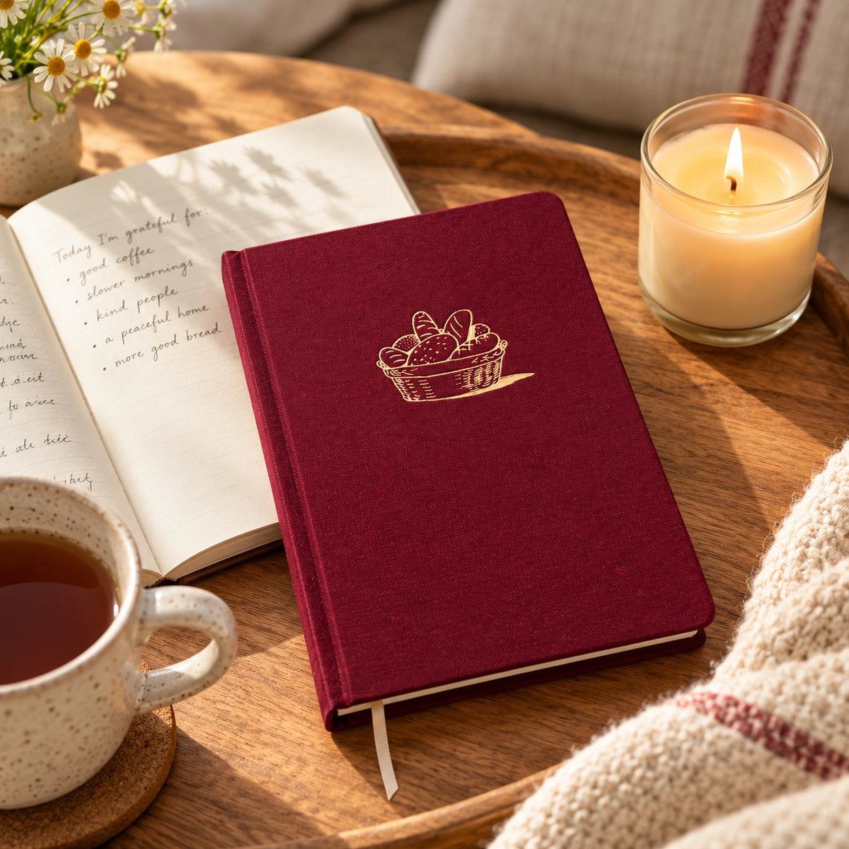 Provided Bread and Wine red fabric journal styled on a wooden tray with an open notebook, tea and candle.