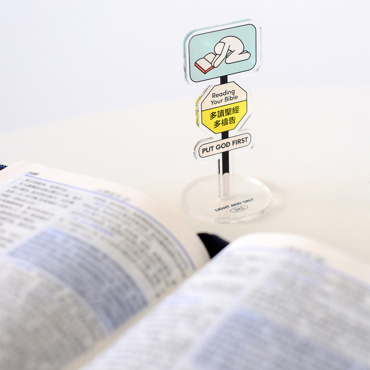 Reading Your Bible acrylic sign with 'Put God First' message displayed on a desk next to an open Bible, promoting Christian devotion.