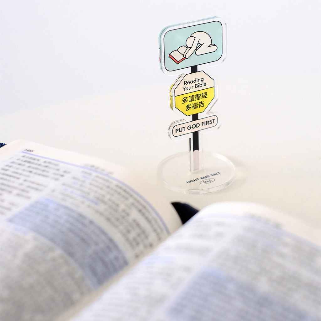 Reading Your Bible acrylic sign with 'Put God First' message displayed on a desk next to an open Bible, promoting Christian devotion.