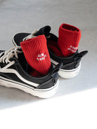 Red cotton socks with white embroidery reading “Always Hallelujah” and “Always Be Grateful” placed beside black sneakers on a light gray surface — a daily faith reminder.