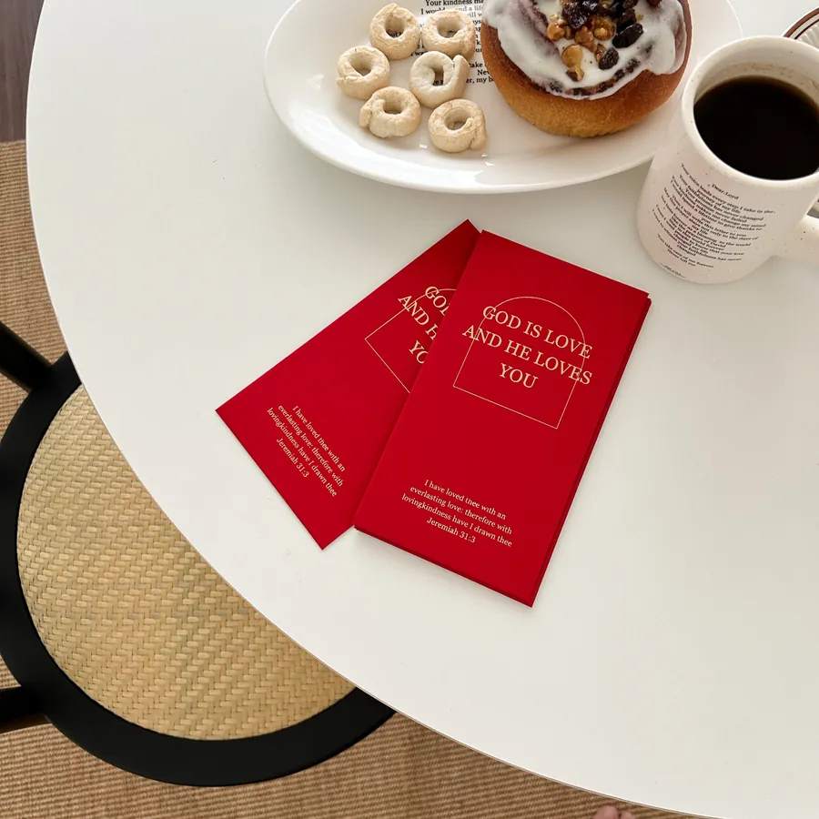 Red packets with the message "God is love and He loves you" displayed on a coffee table alongside pastries and a cup of coffee.
